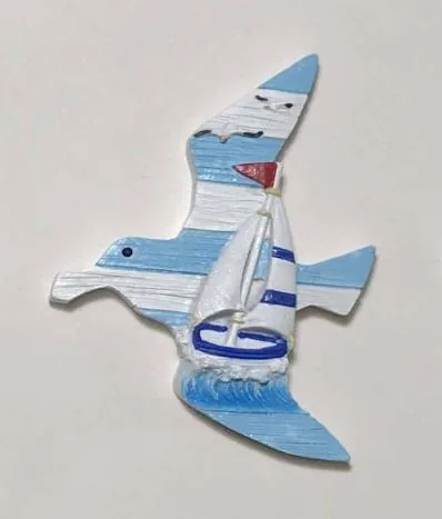 Resin souvenir magnet of a flying seagull with a sailboat, painted in blue and white.