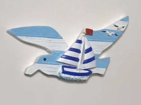 Resin souvenir magnet of a seagull carrying a sailboat over painted driftwood.