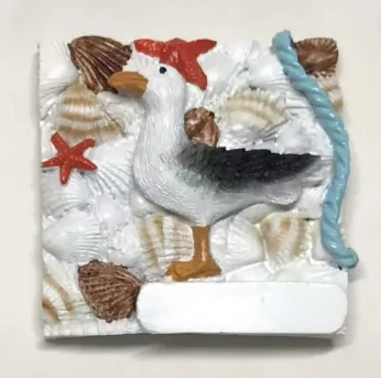 Resin souvenir magnet tile of a seagull among shells and starfish with a blank name plate.