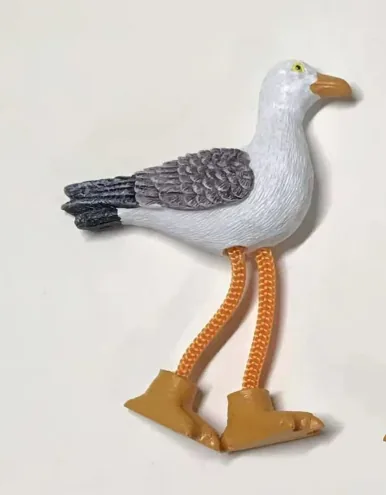 Resin souvenir magnet of a standing seagull in profile with dangling rope legs.