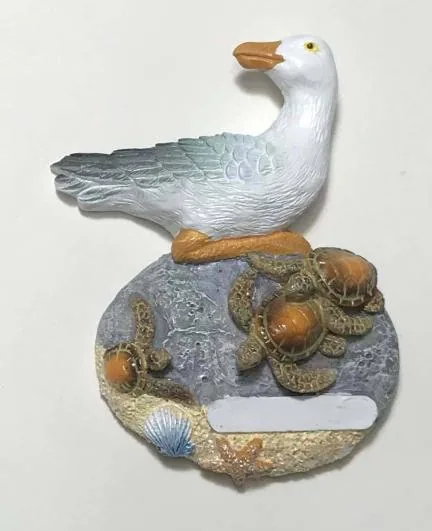 Resin souvenir magnet of a seagull standing over turtles on a rock, with a blank name plate.