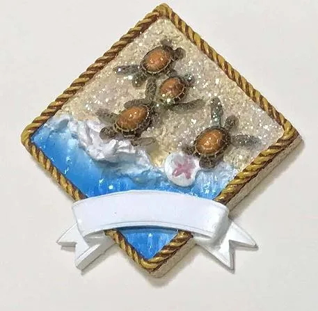 Rope-framed resin souvenir magnet of turtle hatchlings on sand, with a blank white banner.